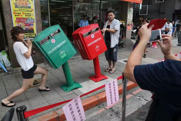 A couple poses for photographs next to a pair of roadside mailboxes that were uniformly bent by a falling signboard during a typhoon earlier this month in Taipei, Taiwan.