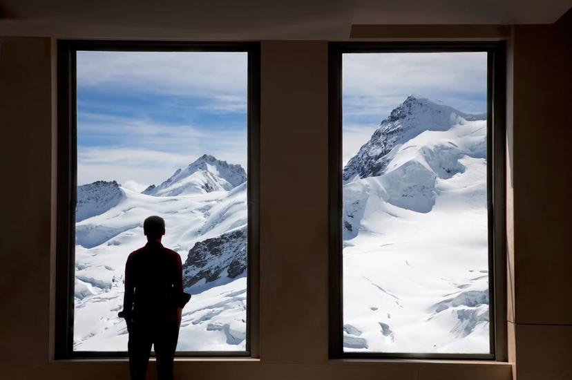 Young man looking out at glaciers at Jungfraujoch through windows.